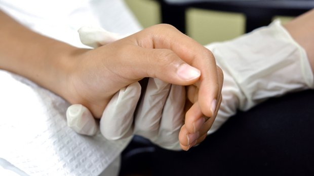 Pfleger hält Hand von Person im Krankenbett
